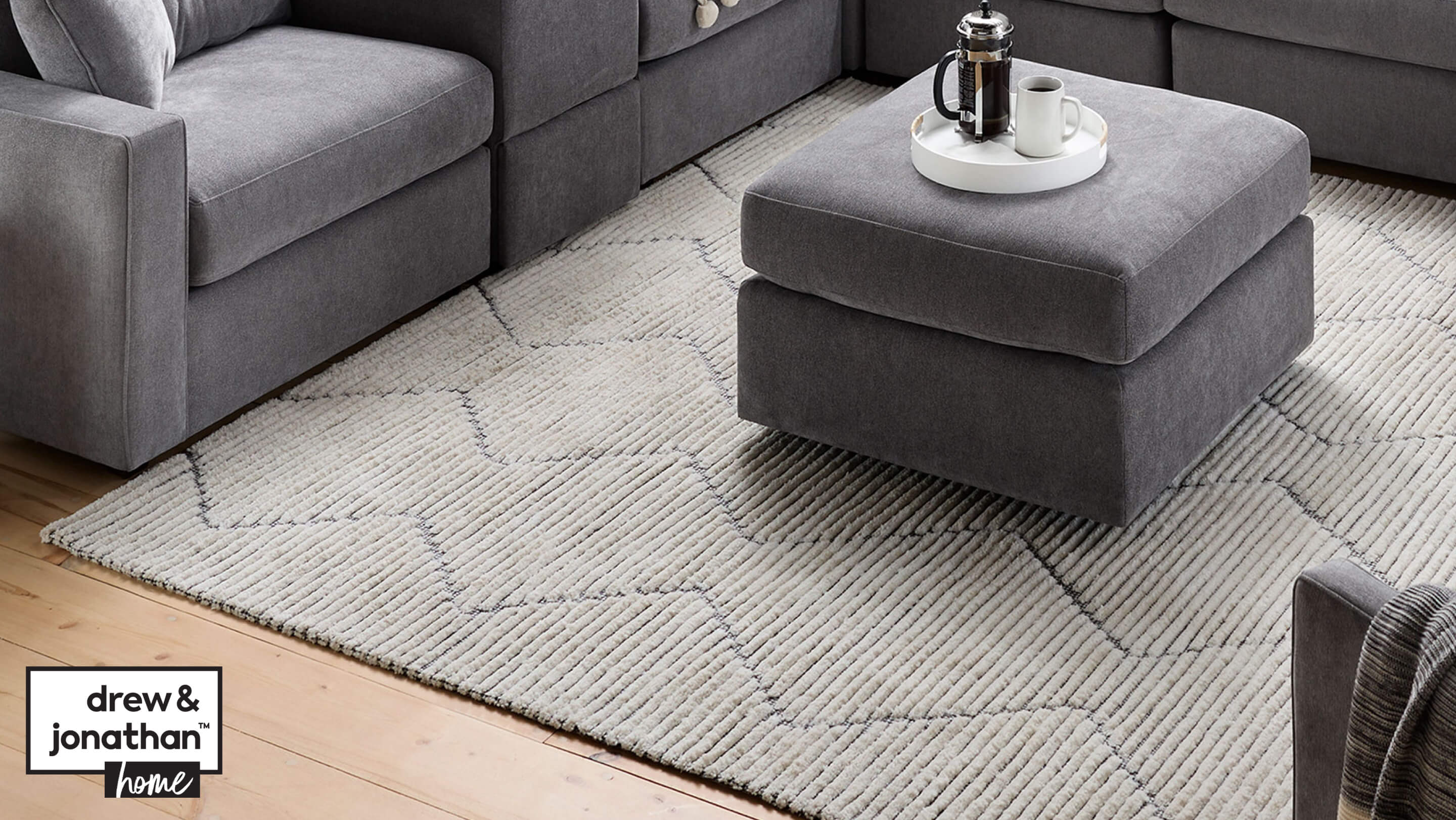 Gray and Ivory abstract Calisto area rug, with gray ModularOne sectional and ottoman. Ottoman has french press coffee maker and white mug on top of it.
