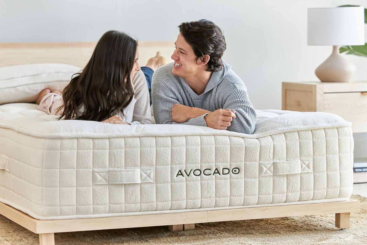Luxury organic avocado mattress with a man and woman on top of the bed, with a light wood bed frame.